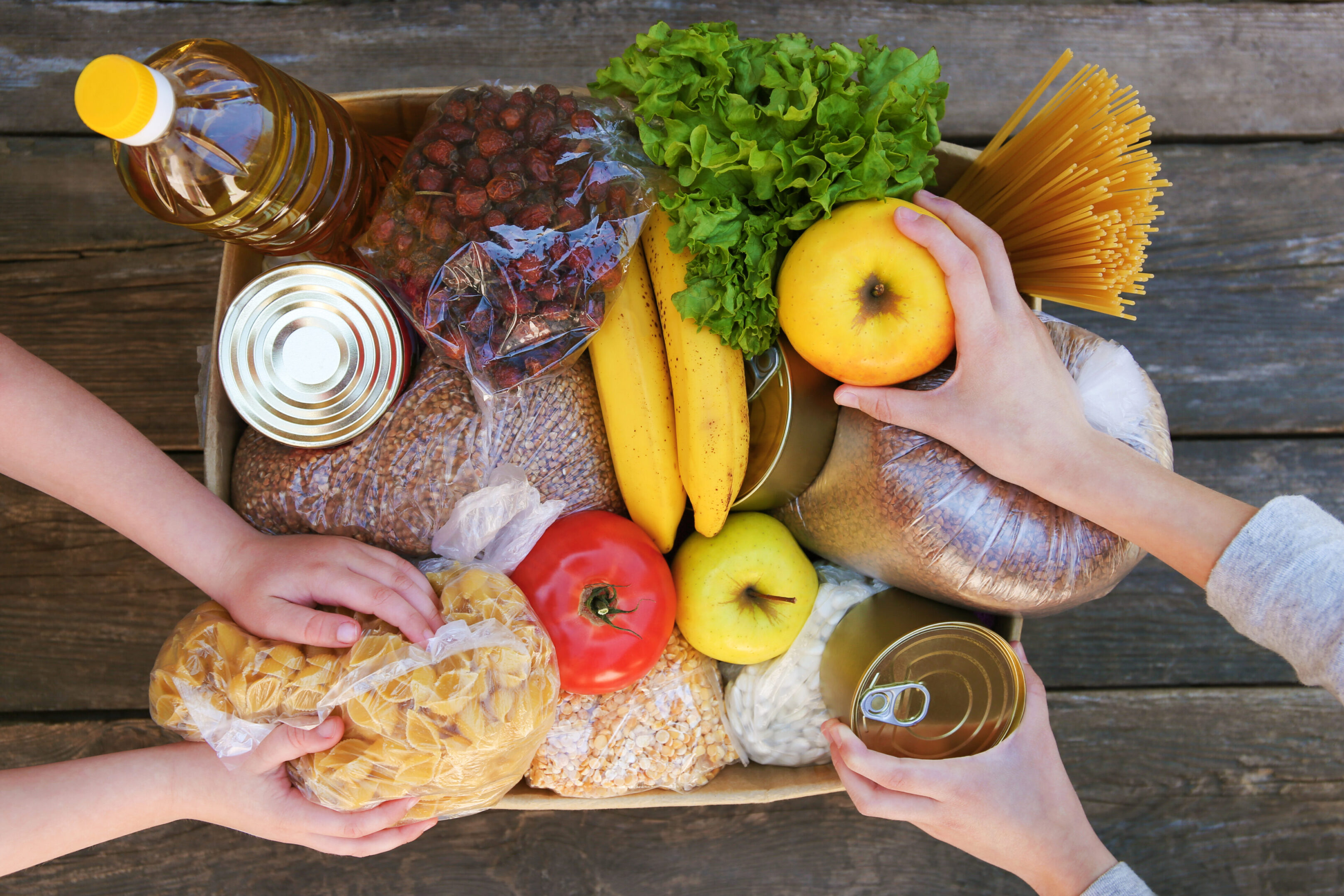 Hands arranging assorted food items in box.