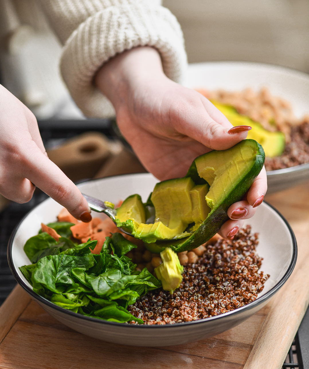 Person preparing avocado quinoa salad bowl.