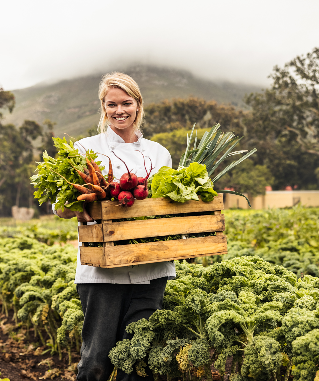 Woman holding crate of fresh vegetables outdoors.