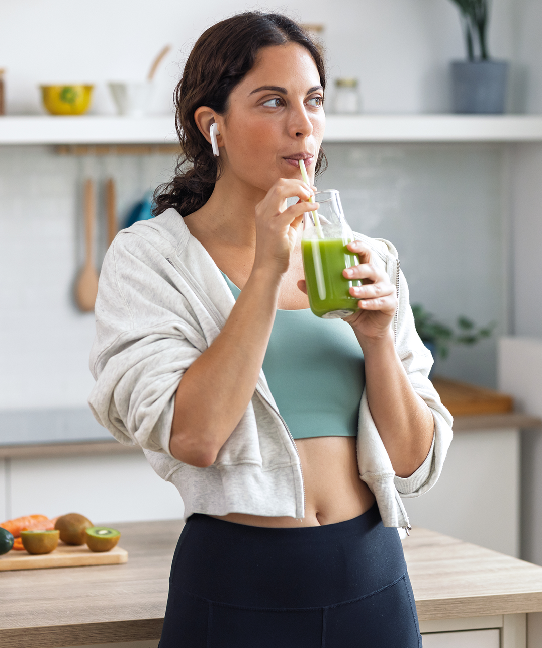 Woman drinking green smoothie in kitchen.