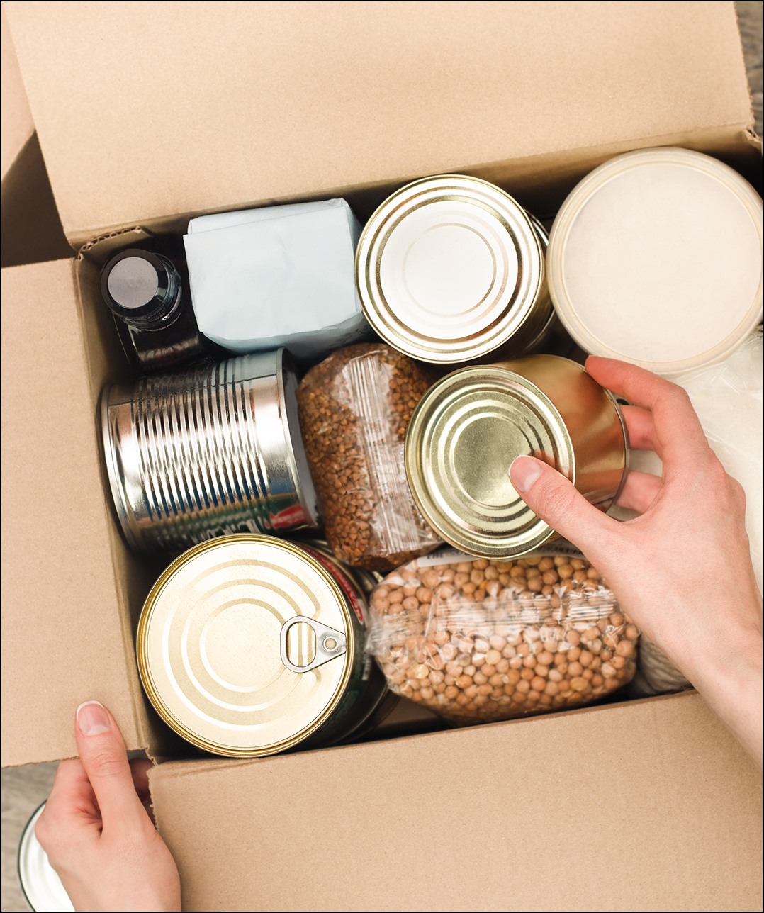 Hands holding canned goods in a box.