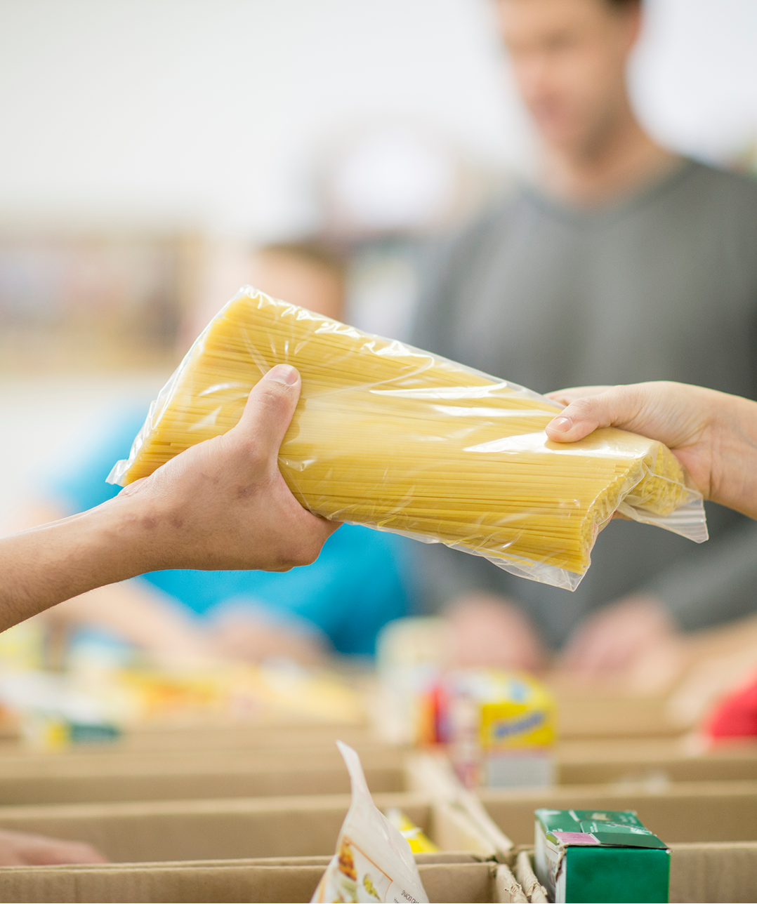 Hands exchanging packaged spaghetti at food bank.