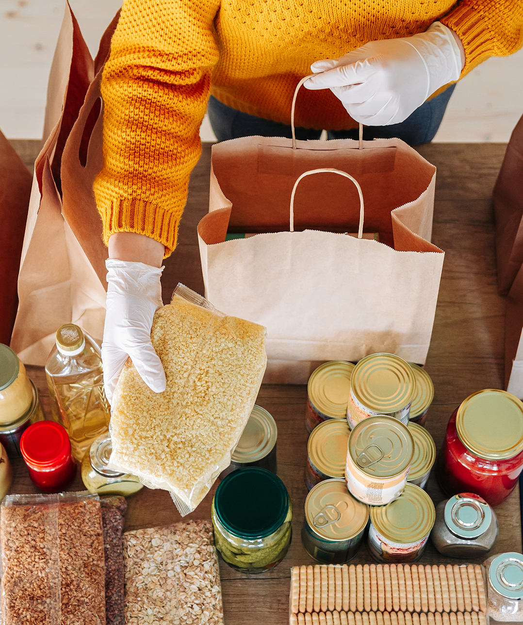 Packing groceries into paper bags, wearing gloves.